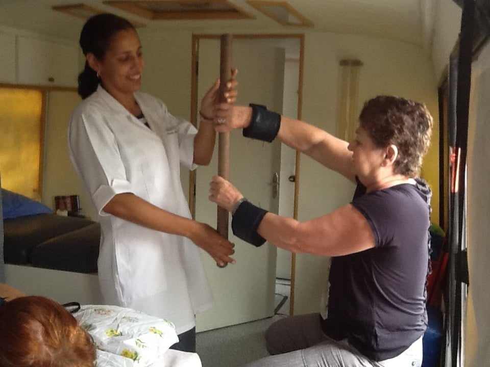 Paciente faz exercícios com um bastão, sob o olhar de uma das fisioterapeutas. A sessão custa 18 reais, para quem puder pagar.