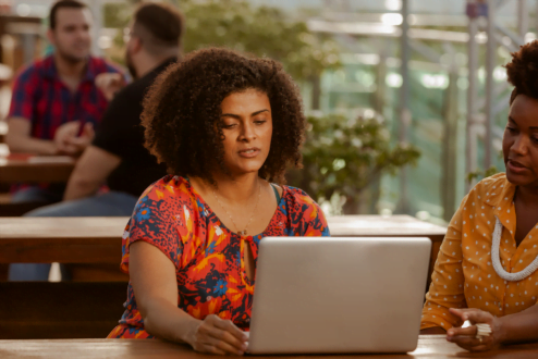 Duas mulheres negras, colaboradoras do CESAR, trabalham juntas em frente ao computador.