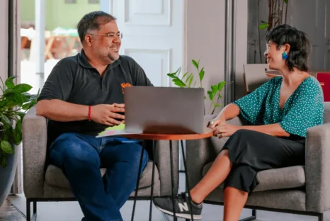 Um homem e uma mulher, colaboradores do CESAR, conversam sentados em frente a um computador.